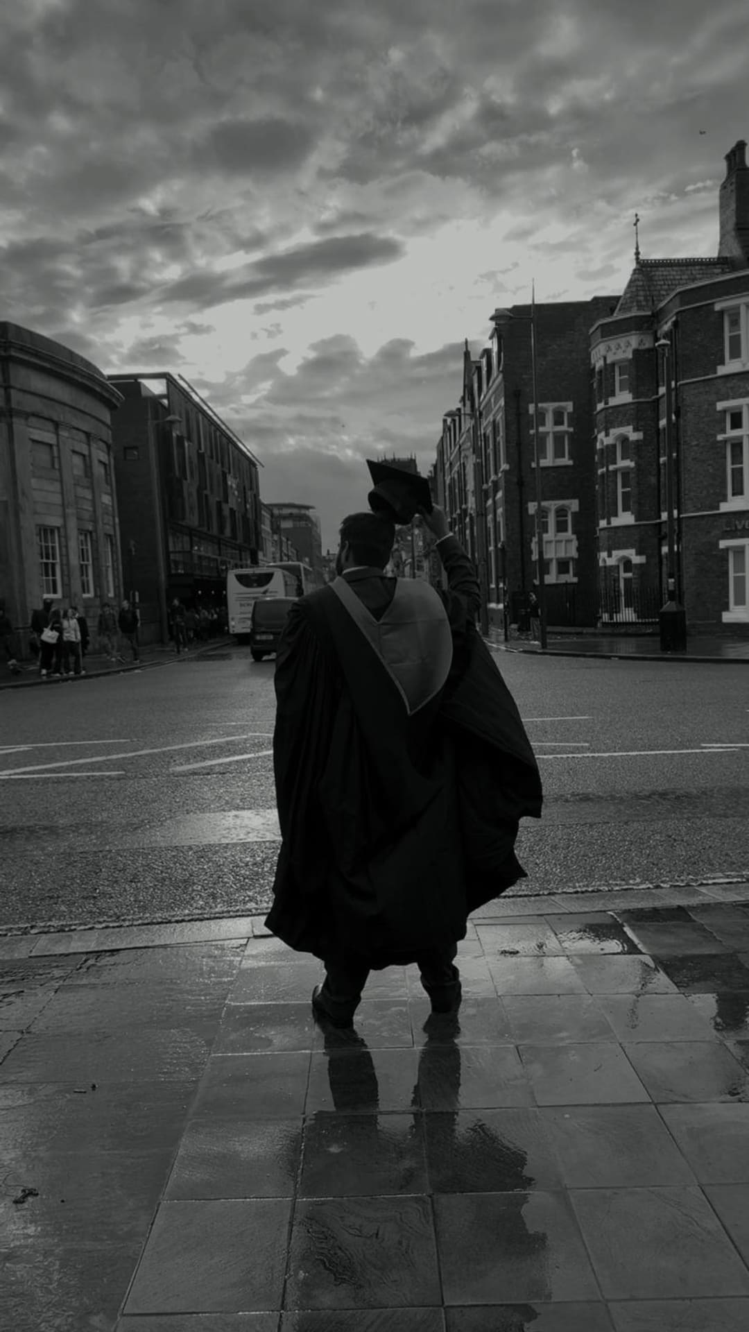 Omkar from behind, holding his graduation cap up to a stormy Liverpool sky