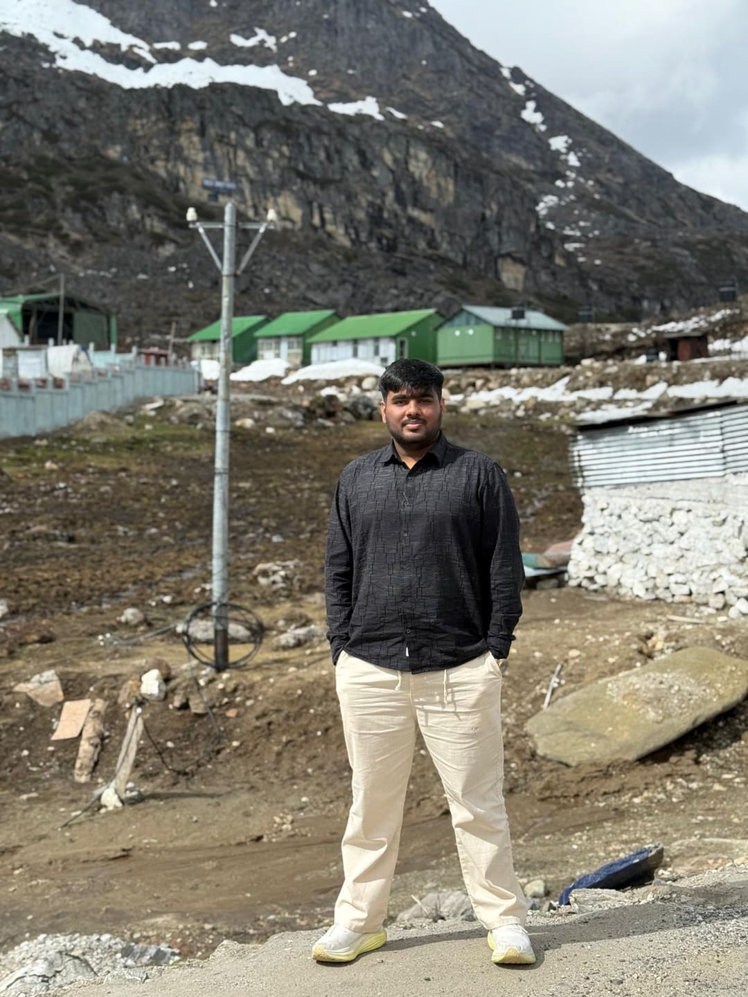 Omkar in front of snow patched mountains and green huts in Arunachal Pradesh